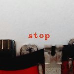 Close-up of a vintage typewriter typing the word 'stop' in red on white paper.