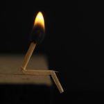 A creative capture of a bent matchstick with a burning flame against a dark backdrop.