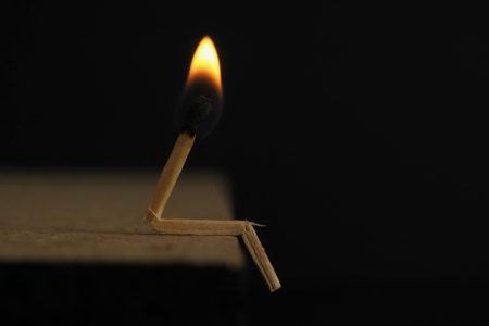 A creative capture of a bent matchstick with a burning flame against a dark backdrop.