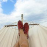 Feet resting on a hammock with red sneakers, epitomizing summer relaxation and leisure outdoors.