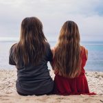 2 women sitting on beach during daytime